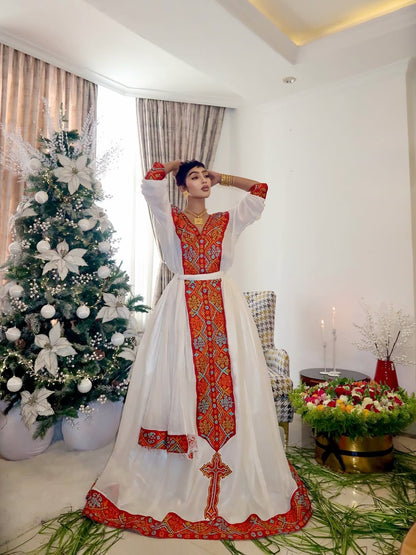 Woman in a traditional Ethiopian traditional dress standing in a decorated room with a Christmas tree and flowers.