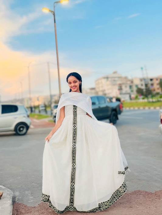 Woman in a white Traditional Dress  with black patterns standing on a street.