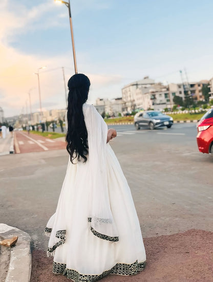 Woman in a white Traditional Dress with black details walking on a street.