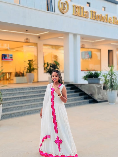 Woman in a white Habesha libs with pink accents standing in front of a hotel entrance.