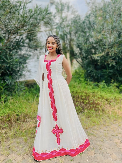 Woman in a white and pink Habesha libs standing outdoors with greenery in the background