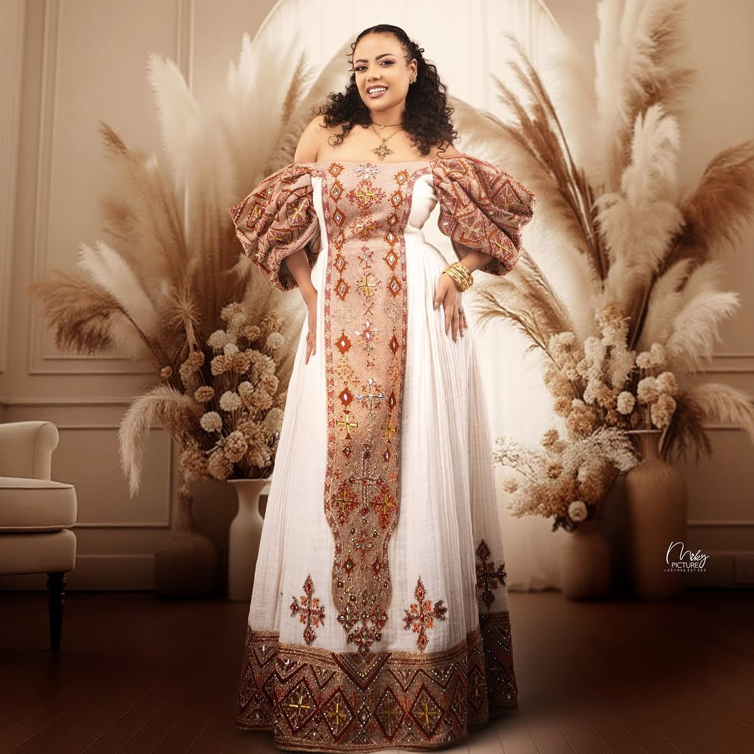 Woman in an ornate Ethiopian Dress   standing in a decorated room with pampas grass and flowers.