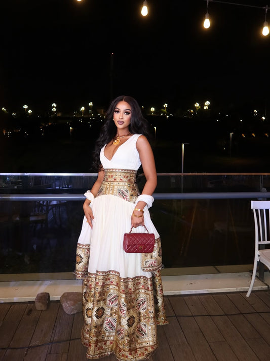 Woman in a white and gold Ethiopia  Kemis with a red handbag standing on a rooftop at night.