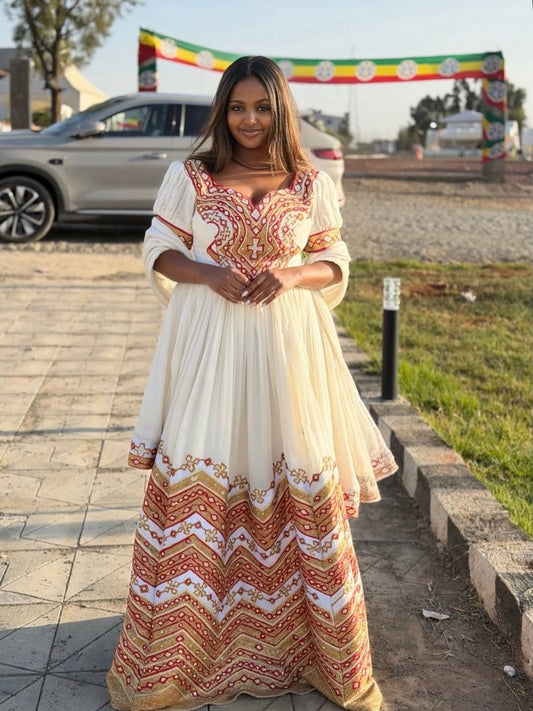 Woman in a long, patterned Eritrean Dressstanding outdoors with a car and colorful banner in the background.