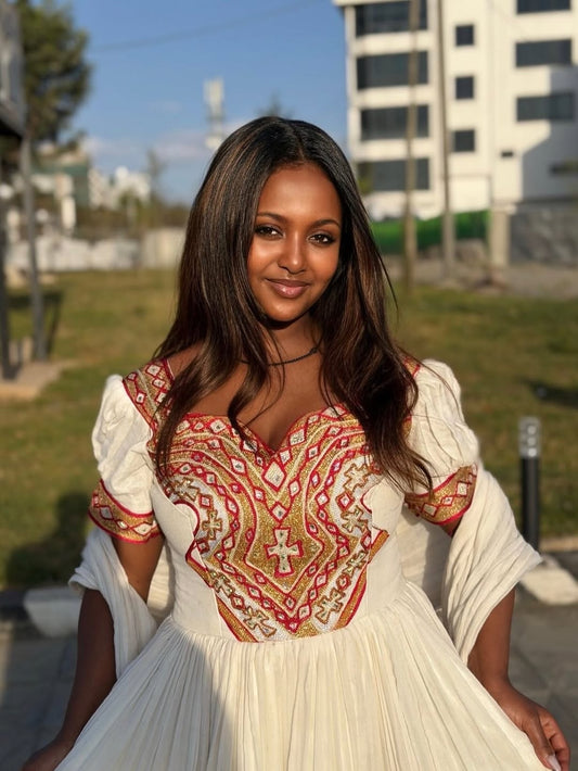 Woman wearing a white Eritrean Dresswith red and gold embroidery outdoors.