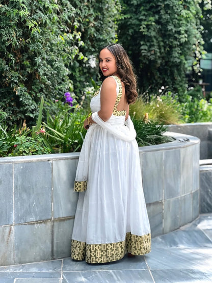 Woman in a white and gold traditional outfit standing in a garden setting.