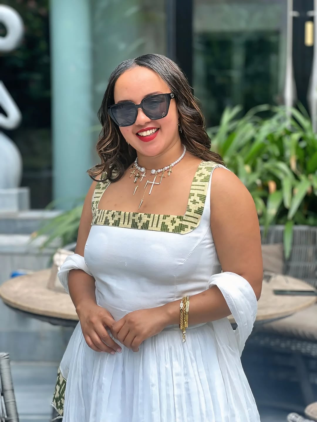 Woman in a white dress with gold accents and sunglasses outdoors.