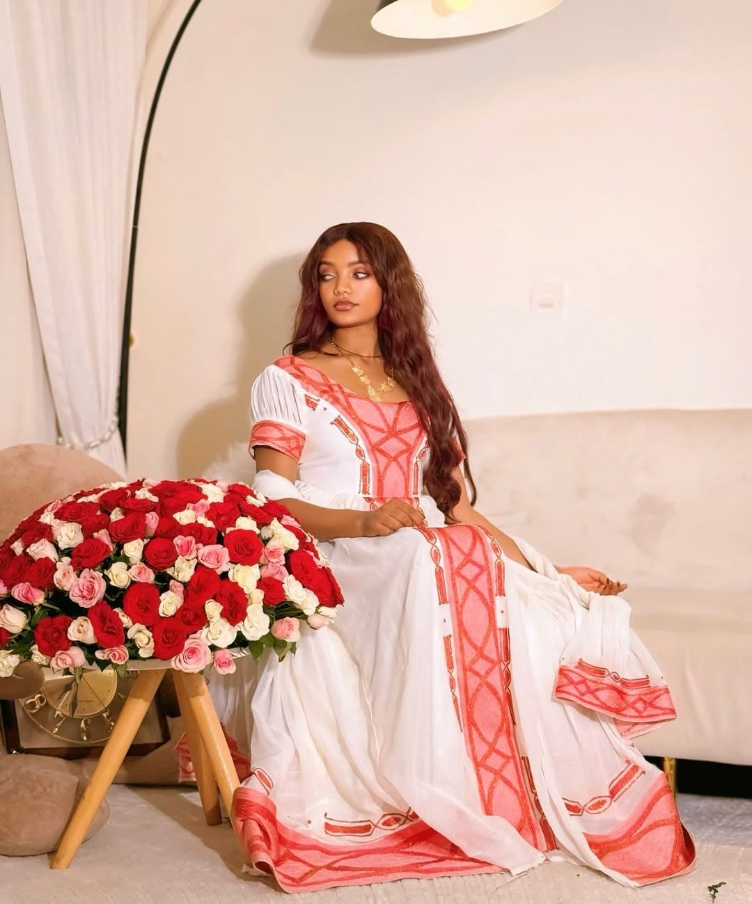 Woman in a white and pink traditional outfit sitting next to a large bouquet of flowers.