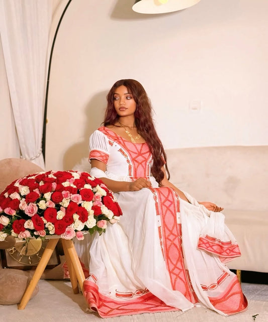 Woman in a white and pink traditional outfit sitting next to a large bouquet of flowers.