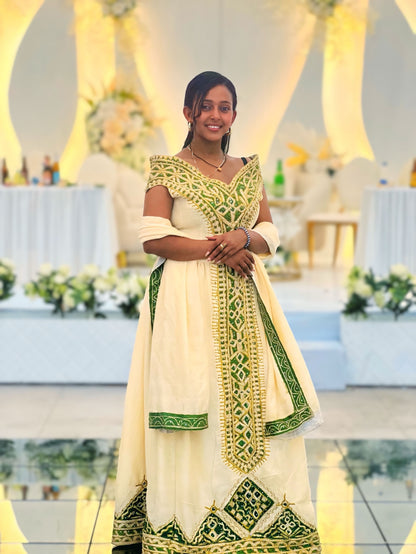 A woman wearing a traditional Indian salwar Ethiopian National Dresses in off-white with green and gold embroidery, standing in a decorated event hall.