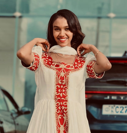 Woman in a white Red Habesha Kemis with red embroidery standing in front of a blurred background