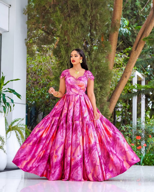 Woman in a pink habesha chiffion standing outdoors with greenery in the background