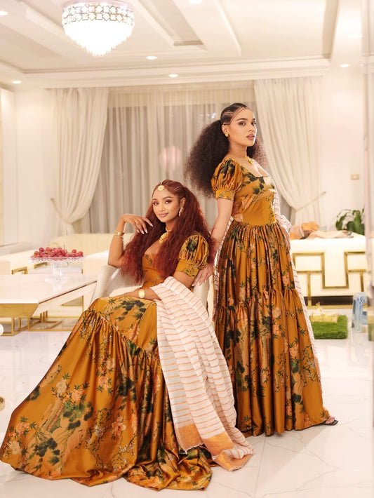 Two women in matching floral habesha shiffon posing in a stylish room.