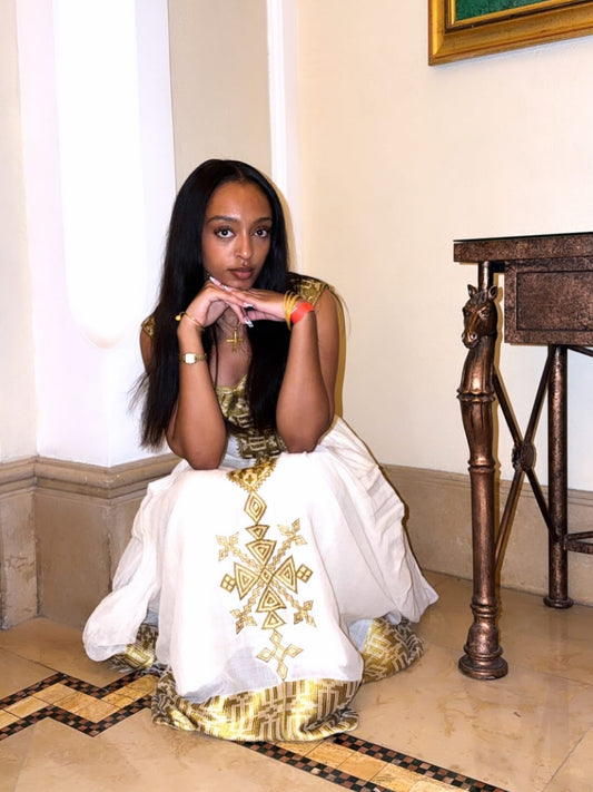 Woman in a white and gold traditional habesh kemis sitting on a marble floor. 