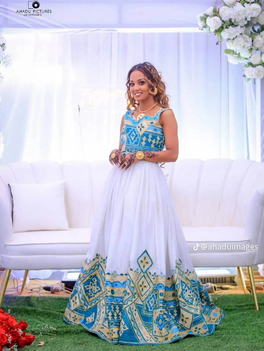 Woman in a blue and white traditional habesha wedding dress standing in front of a decorated setup with flowers.