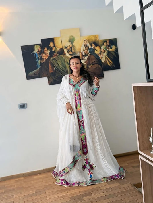 Woman in a Purple Habesha Zuria with colorful embroidery standing in a room with paintings on the wall.