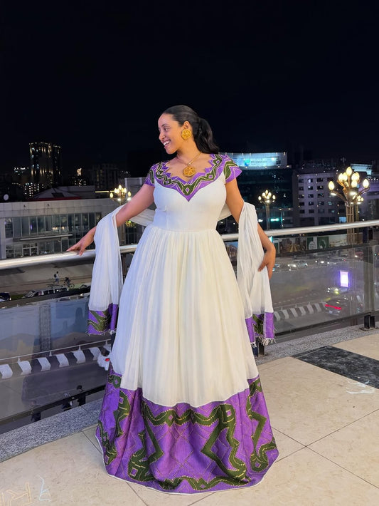 Woman in a white and purple traditional outfit with green patterns on a rooftop at night.