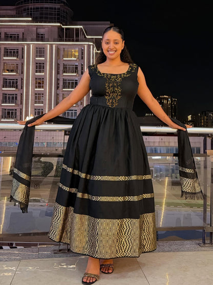 A woman modeling a sleeveless black maxi Habesha zuria with gold embroidery on the bodice and gold patterned borders on the skirt, holding matching black and gold dupatta pieces, set against a nighttime city building background.