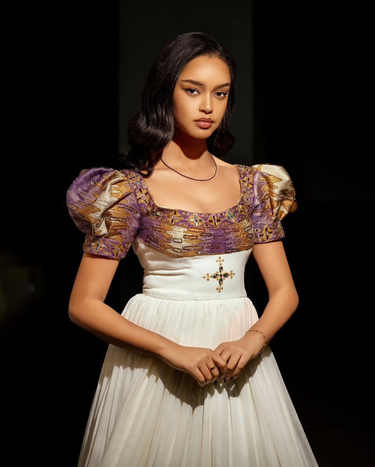 Woman wearing a Habesha wedding Dress with a patterned top and white skirt against a dark background