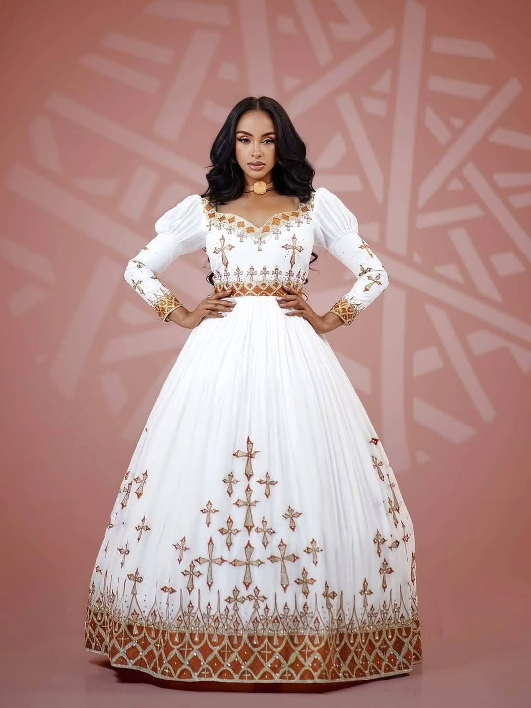 Woman wearing a white and gold embroidered Habesha Dress against a patterned background