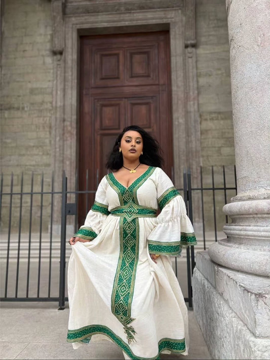 Woman in a white Ethiopian Traditional Dress with green patterns standing in front of a building entrance.