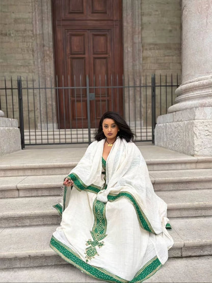 Woman in a white and green embroidered Ethiopian Traditional Dress sitting on steps in front of a building.