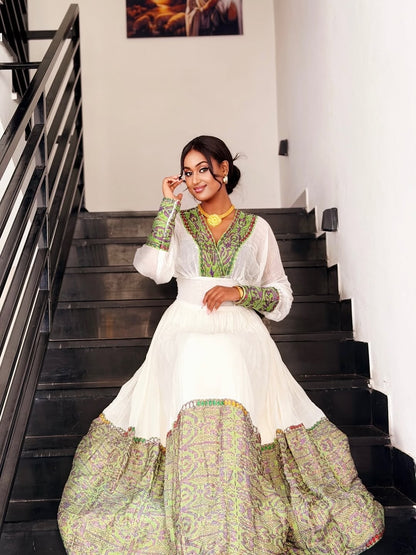 Woman in a white and green traditional Habesha Zuria sitting on stairs.
