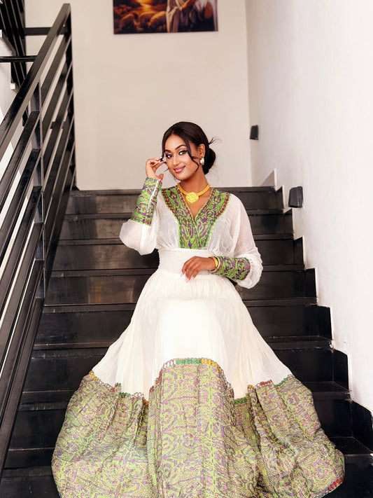Woman in a white and green traditional Habesha Zuria sitting on stairs.