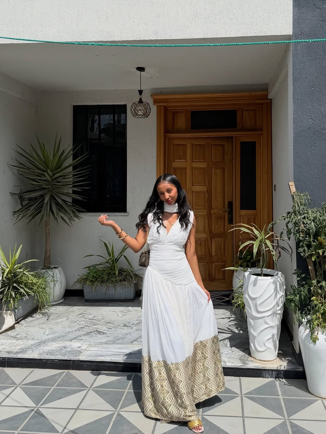 Woman in a white Habesha Dress  standing in front of a house entrance with plants around.