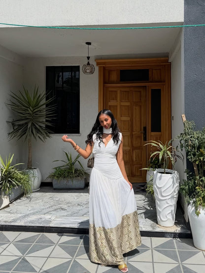 Woman in a white Habesha Dress  standing in front of a house entrance with plants around.