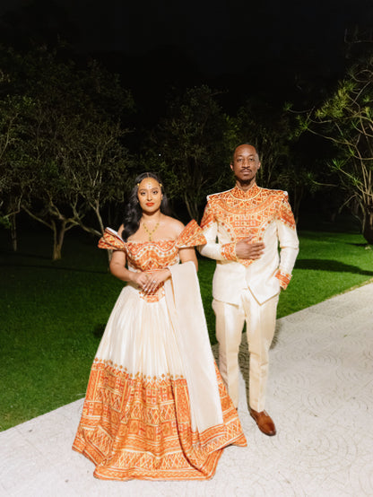 A couple posing in matching off-white traditional Ethiopian matching couple outfit with intricate orange and red embroidered patterns (tibeb).