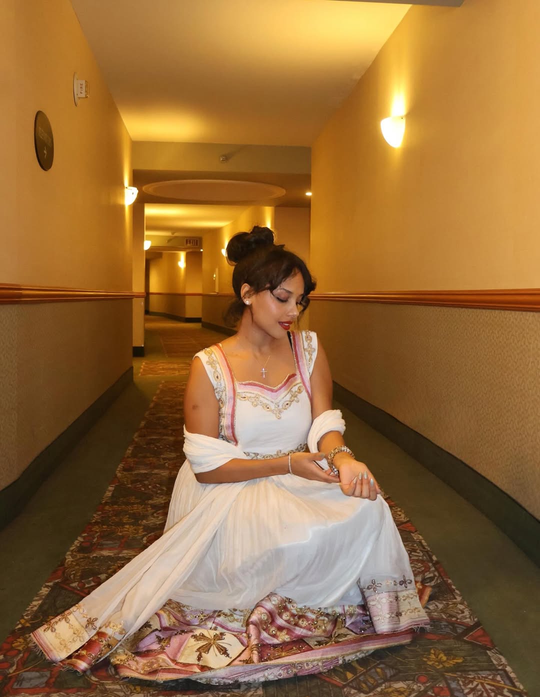 Woman in a white Ethiopian traditional dress  sitting on a patterned rug in a hallway