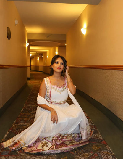Woman in a white Ethiopian traditional dress  sitting on a patterned rug in a hallway.