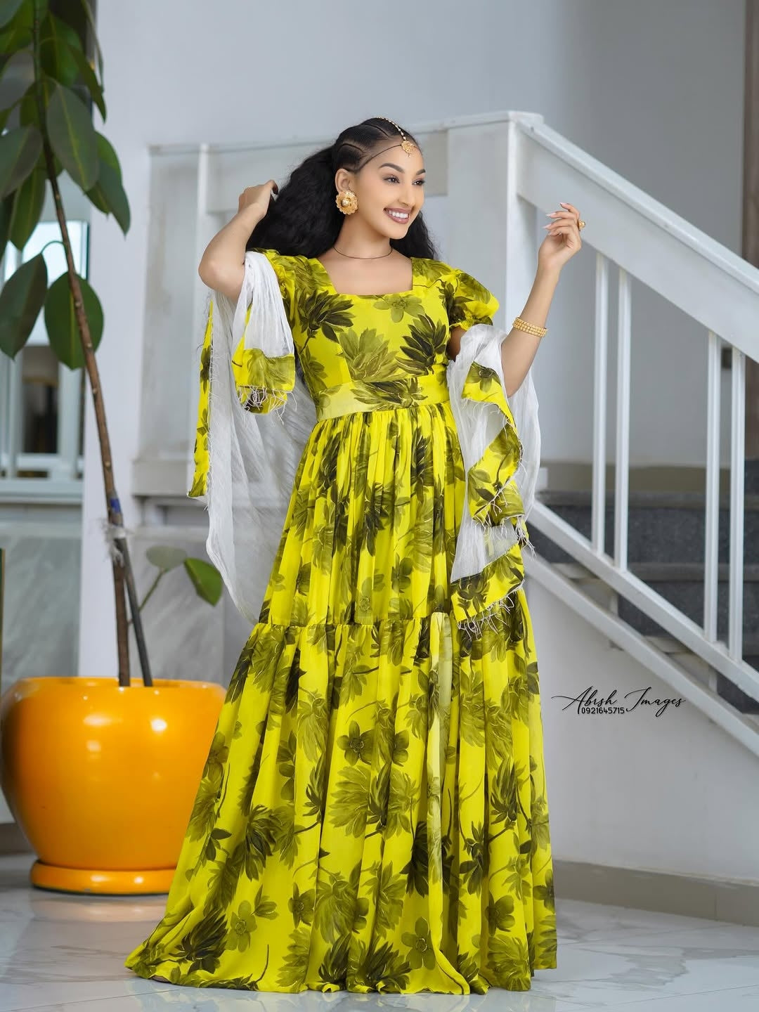 Woman in a Yellow Habesha Shifion standing indoors with a white railing and plant in the background