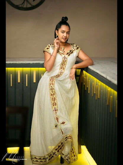 Woman in a white and gold traditional outfit posing in a modern interior setting.