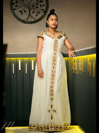 Woman wearing a white dress with gold embroidery in an indoor setting