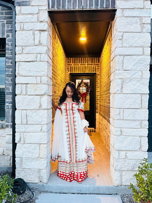 Woman in a white and red Habesha Kemis standing in a stone-walled entranceway.