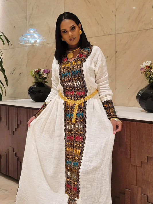 Woman wearing a white Gondar Fetel Dress with colorful embroidery in an indoor setting.