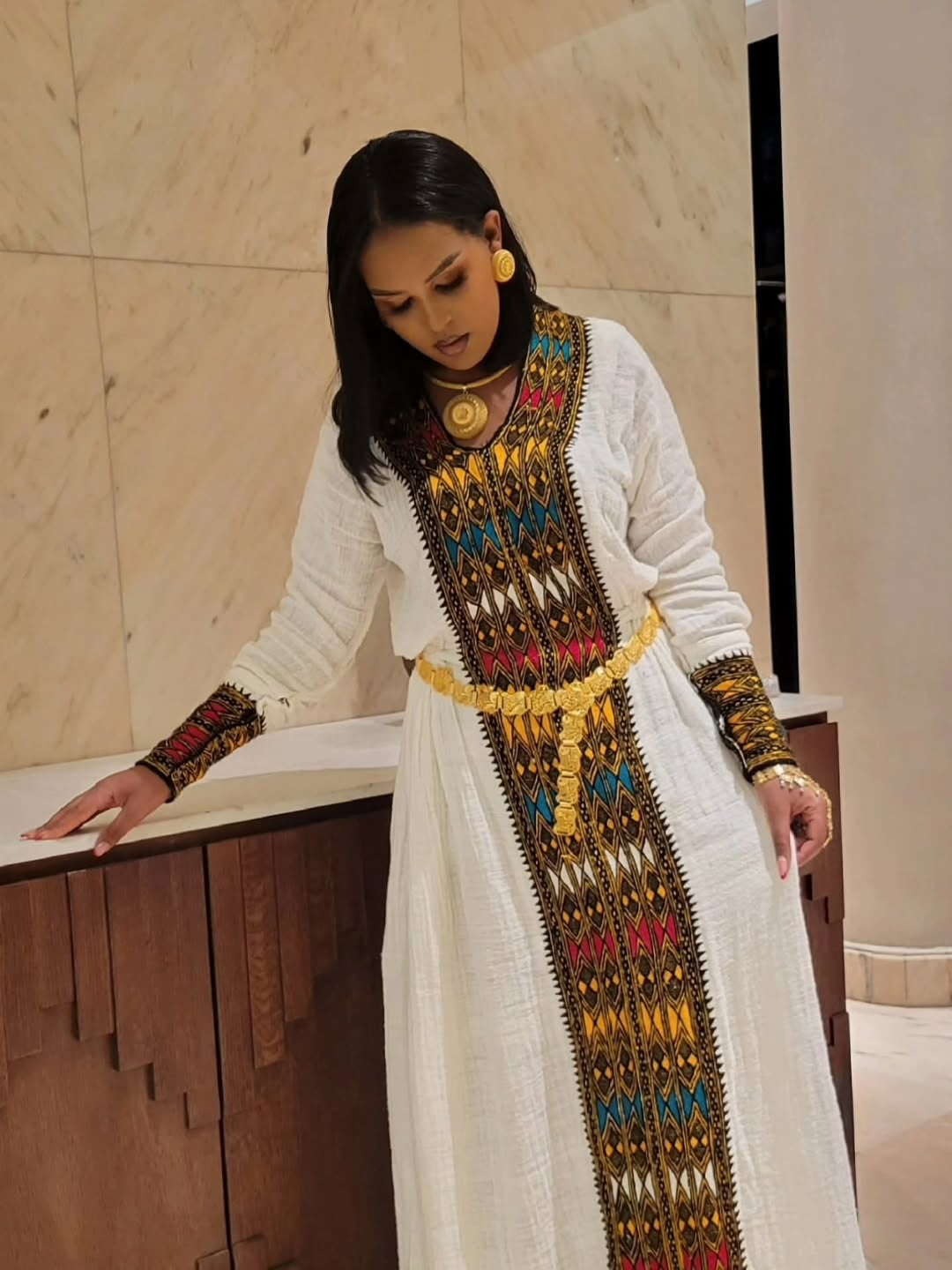 Woman wearing a long, ornate Gondar Fetel Dress with colorful embroidery in an indoor setting.