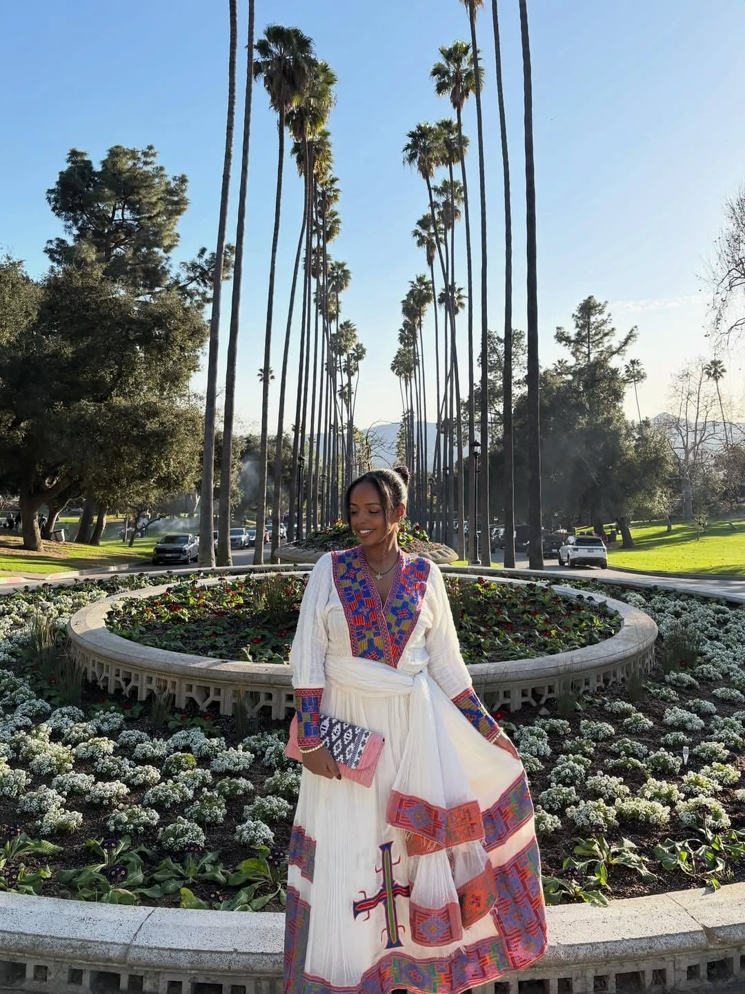 Woman in a colorful dress standing in front of palm trees and manicured gardens.