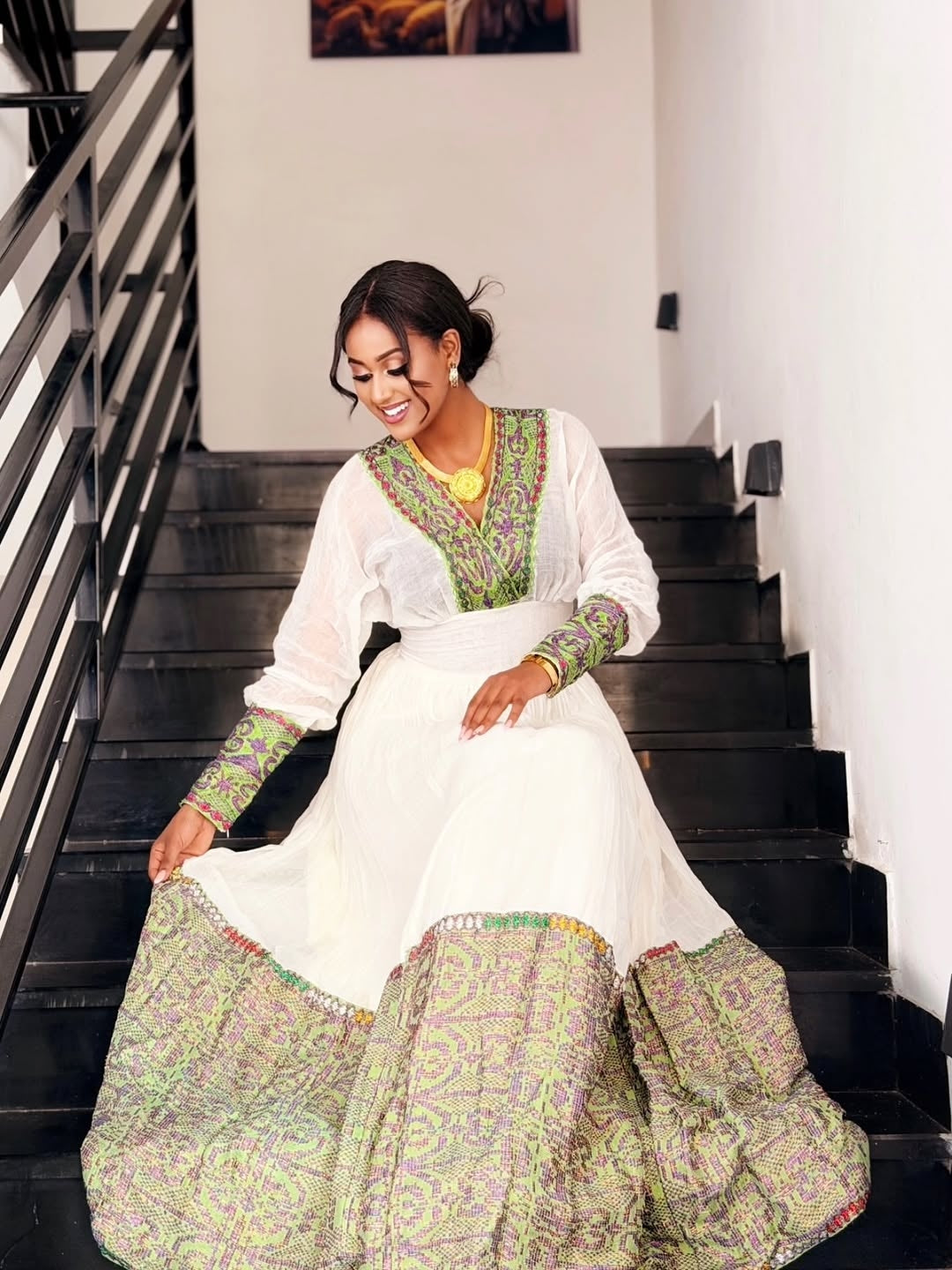 Woman in a white and gold habesha dress in an elegant interior setting.