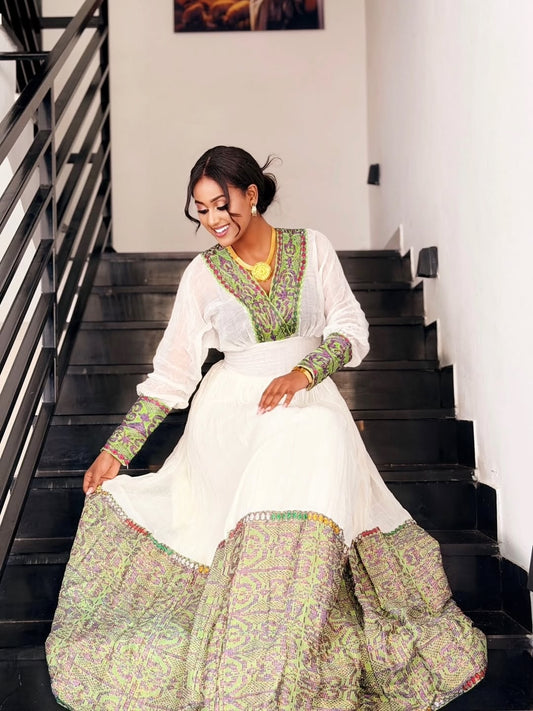 Woman in a white and gold habesha dress in an elegant interior setting.
