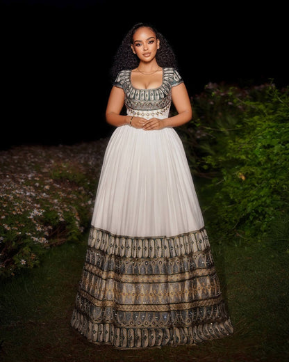 Woman wearing a traditional ethiopian dress with a white skirt and patterned top, standing outdoors.