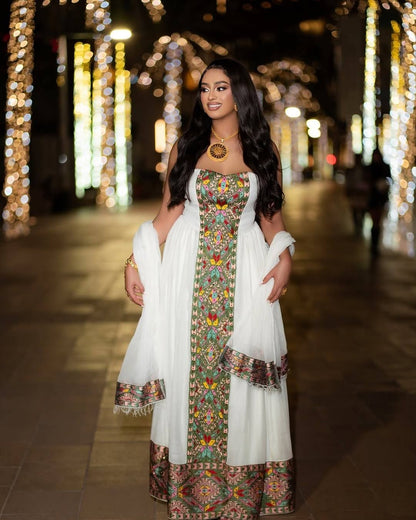 A woman wearing a white traditional habesha kemis  with colorful floral embroidery and a matching white dupatta, standing in a nighttime street setting decorated with warm bokeh lights.