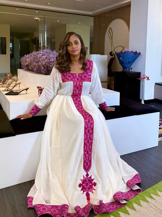 Woman in a white and pink traditional habesha zuria standing in a modern room with decor elements.