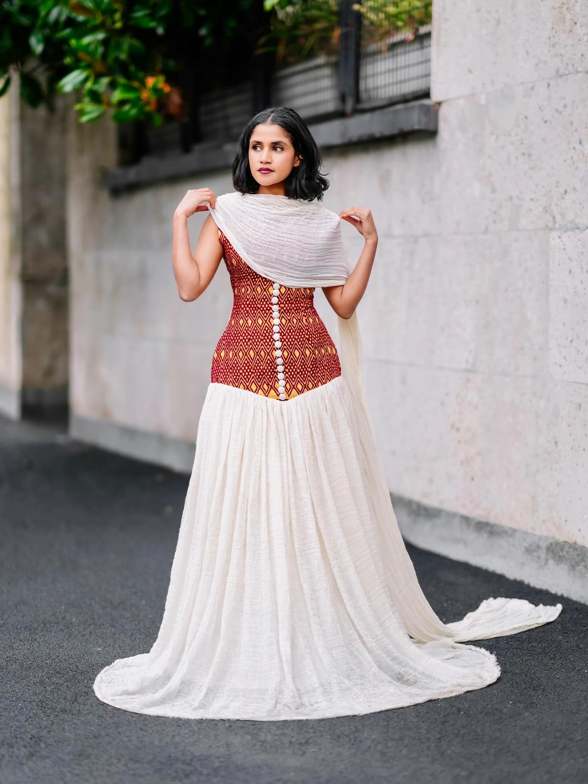 Woman wearing a traditional habesha kemis with a red blouse and white saree, standing against a light-colored wall.