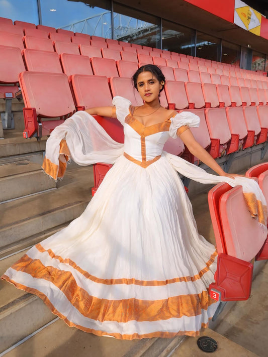 Woman in a white and orange Ethiopian Dress standing in an empty stadium with red seats.