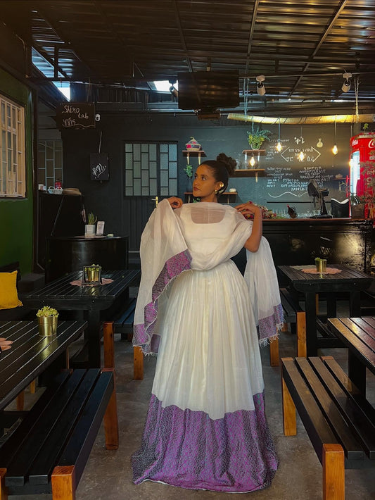 Woman in a white and purple  Habesha Kemis  standing in a restaurant setting