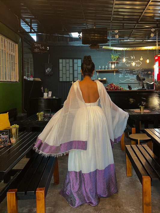 Woman in a white and purple  Habesha Kemis  standing in a restaurant.