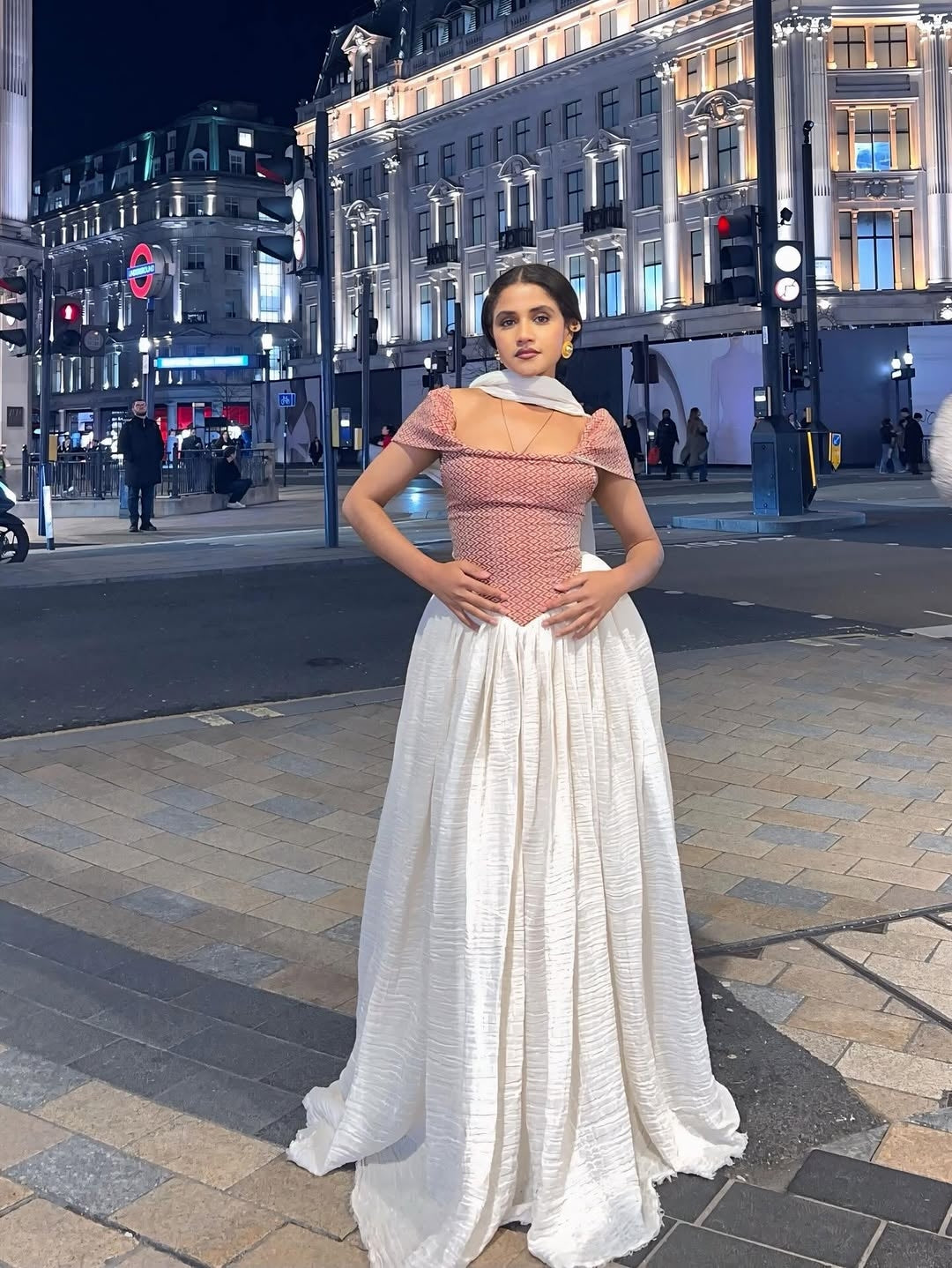 Woman in a red top and white Red Off Shoulder Flowing Habesha Zuria standing on a city street at night.